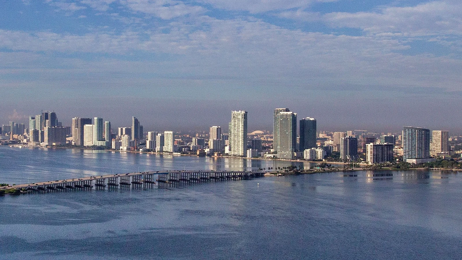 Aerial view across Biscayne Bay to the high-rise towers along the Edgewater waterfront, with a causeway in the foreground; the photo shows the Edgewater neighbourhood, not the 1800 Club building.