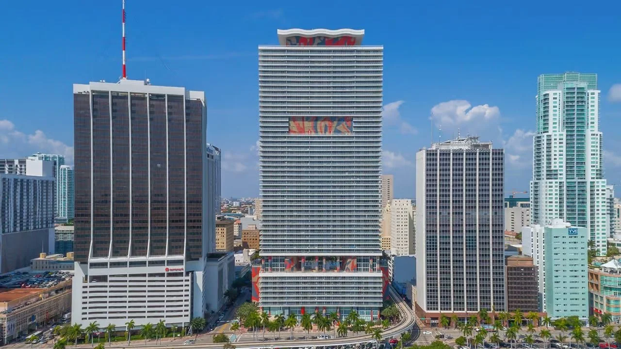The 50 Biscayne condo tower in Downtown Miami, with white horizontal balcony bands and colourful artwork on its facade, between neighbouring office and residential towers.