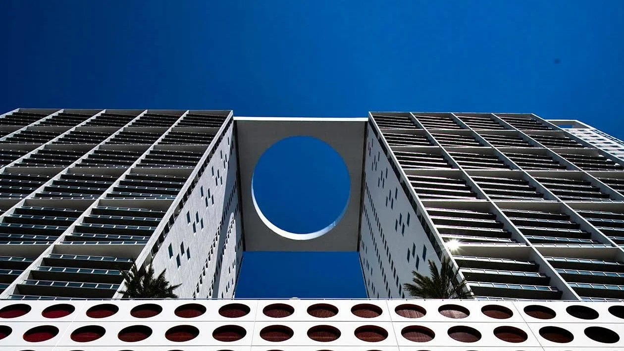 The top of the 500 Brickell twin towers joined by a bridge with a circular opening, against a blue sky.