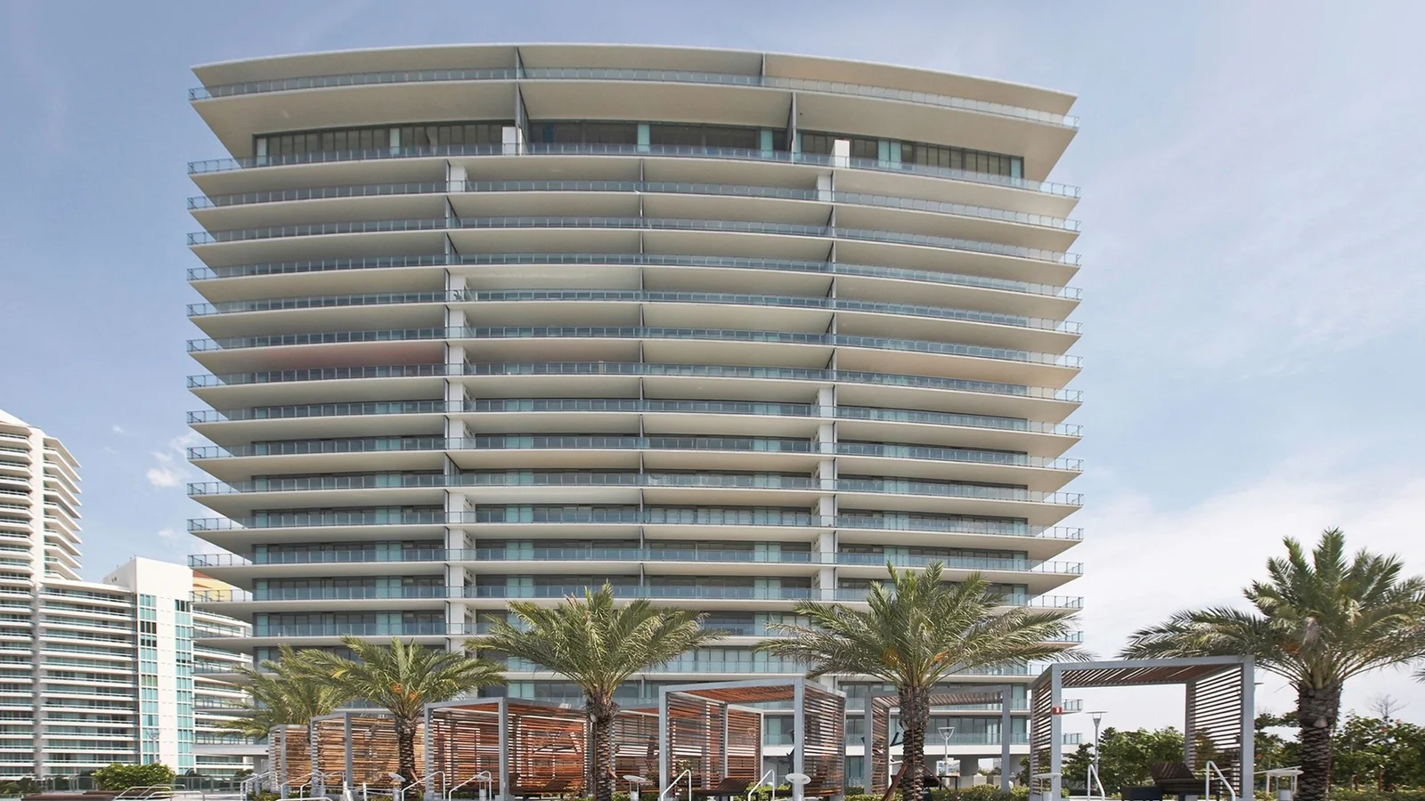 Apogee South Beach tower with curved white balconies, seen from its palm-lined pool deck