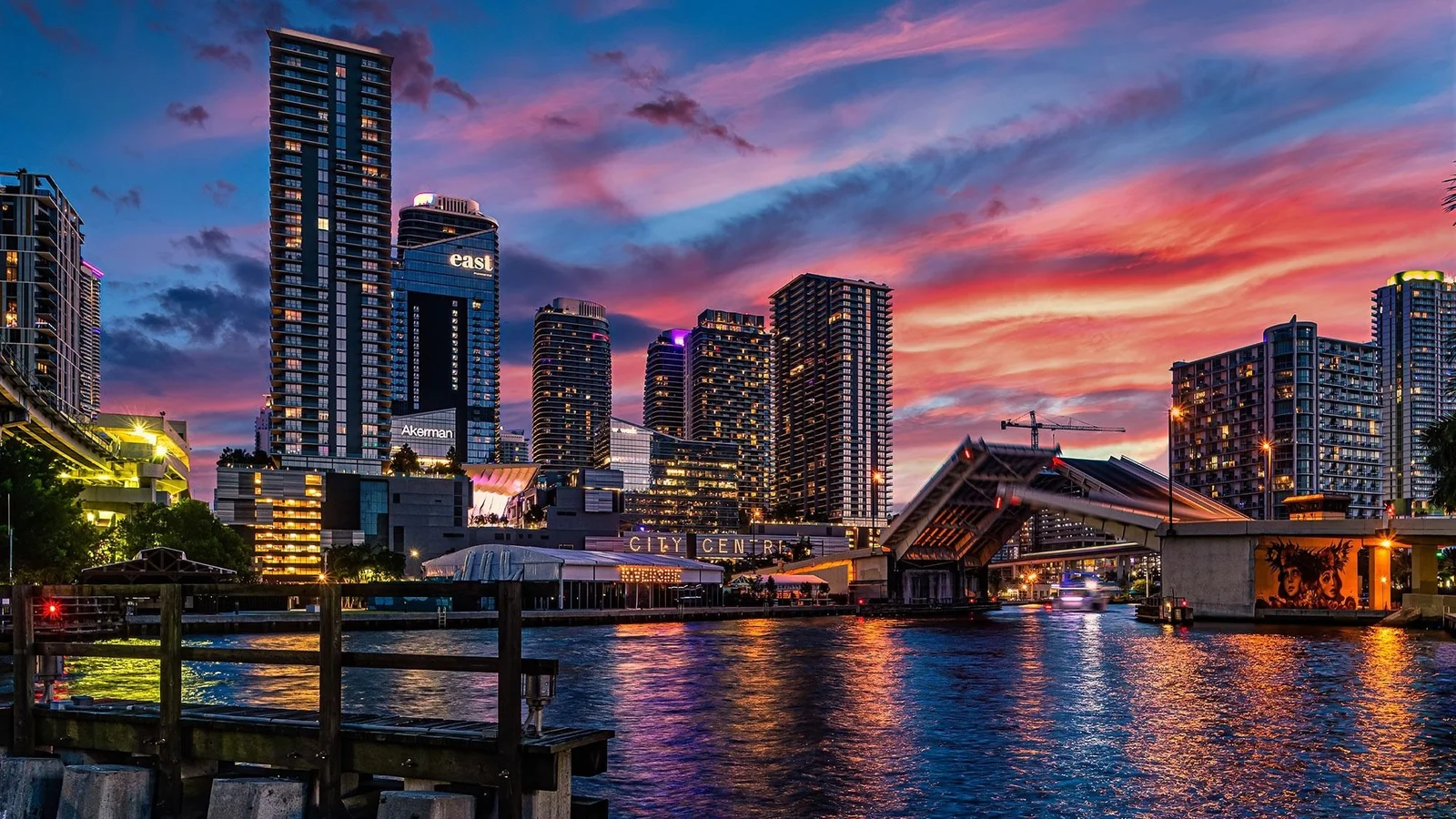 Brickell neighbourhood towers at sunset seen across the Miami River, with the Brickell Avenue Bridge raised; the photo shows the neighbourhood, not Astor Crown.