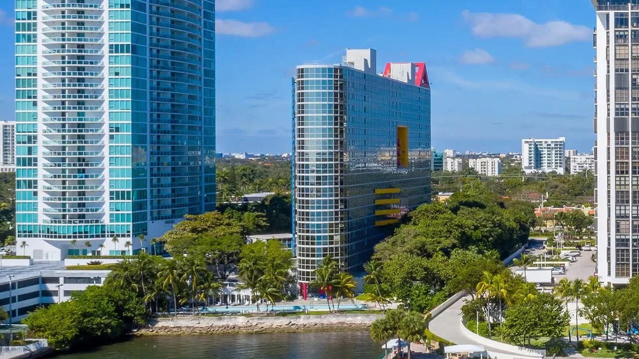 The glass Atlantis on Brickell tower with its red rooftop triangle, seen across the water among Brickell trees and towers.