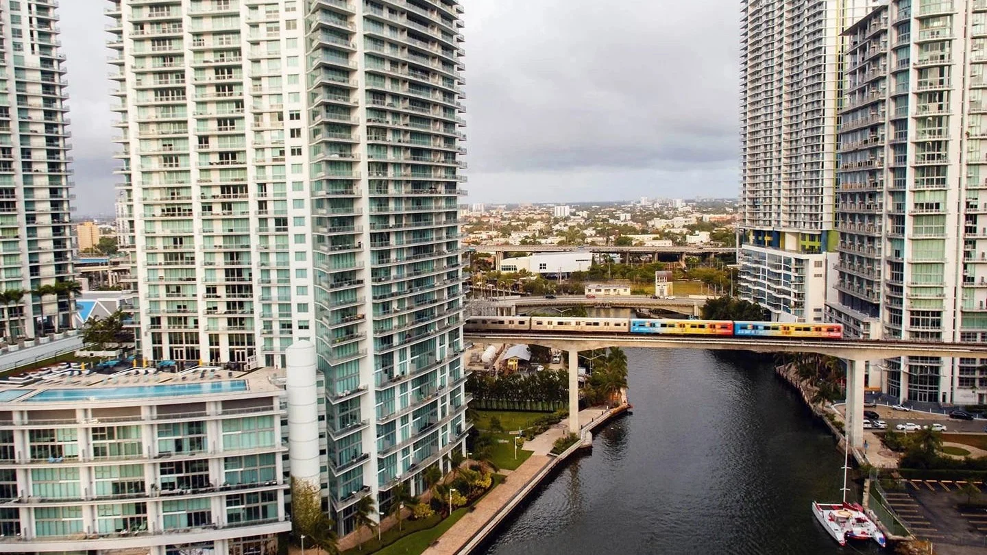 Brickell condo towers on both banks of the Miami River with a Metrorail train crossing