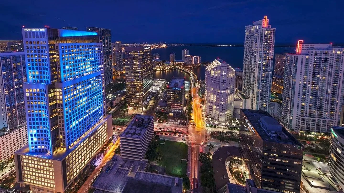 Brickell at night seen from above, with lit office and condo towers leading to Brickell Key; the photo shows the neighbourhood, not Brickell Bay Club.