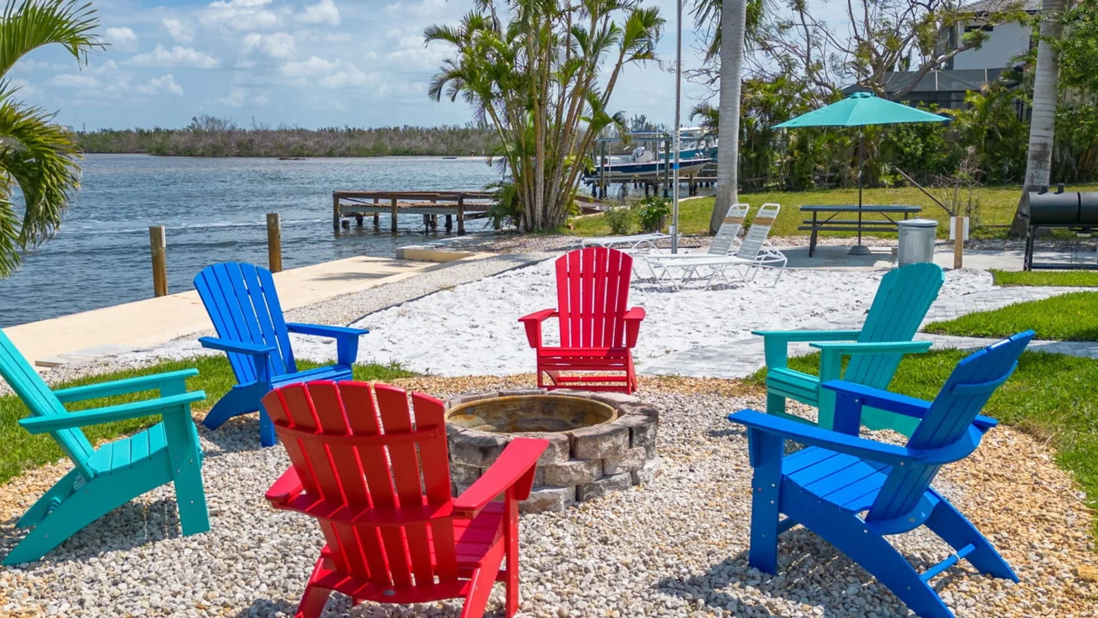 Colorful Adirondack chairs around a fire pit at a waterfront rental home in the Fort Myers area.