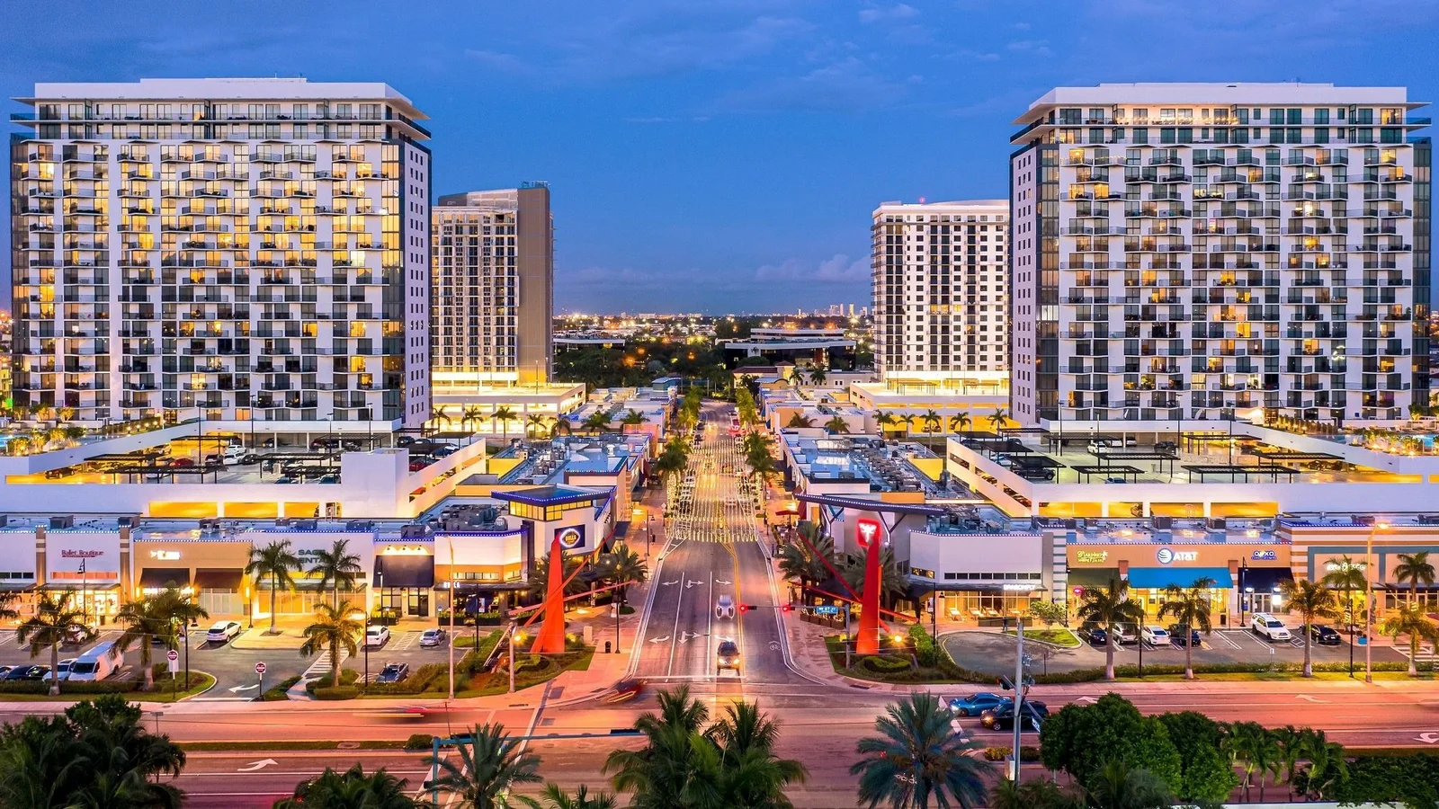 Downtown Doral by Codina Partners at dusk, with residential towers above a lit shopping street.