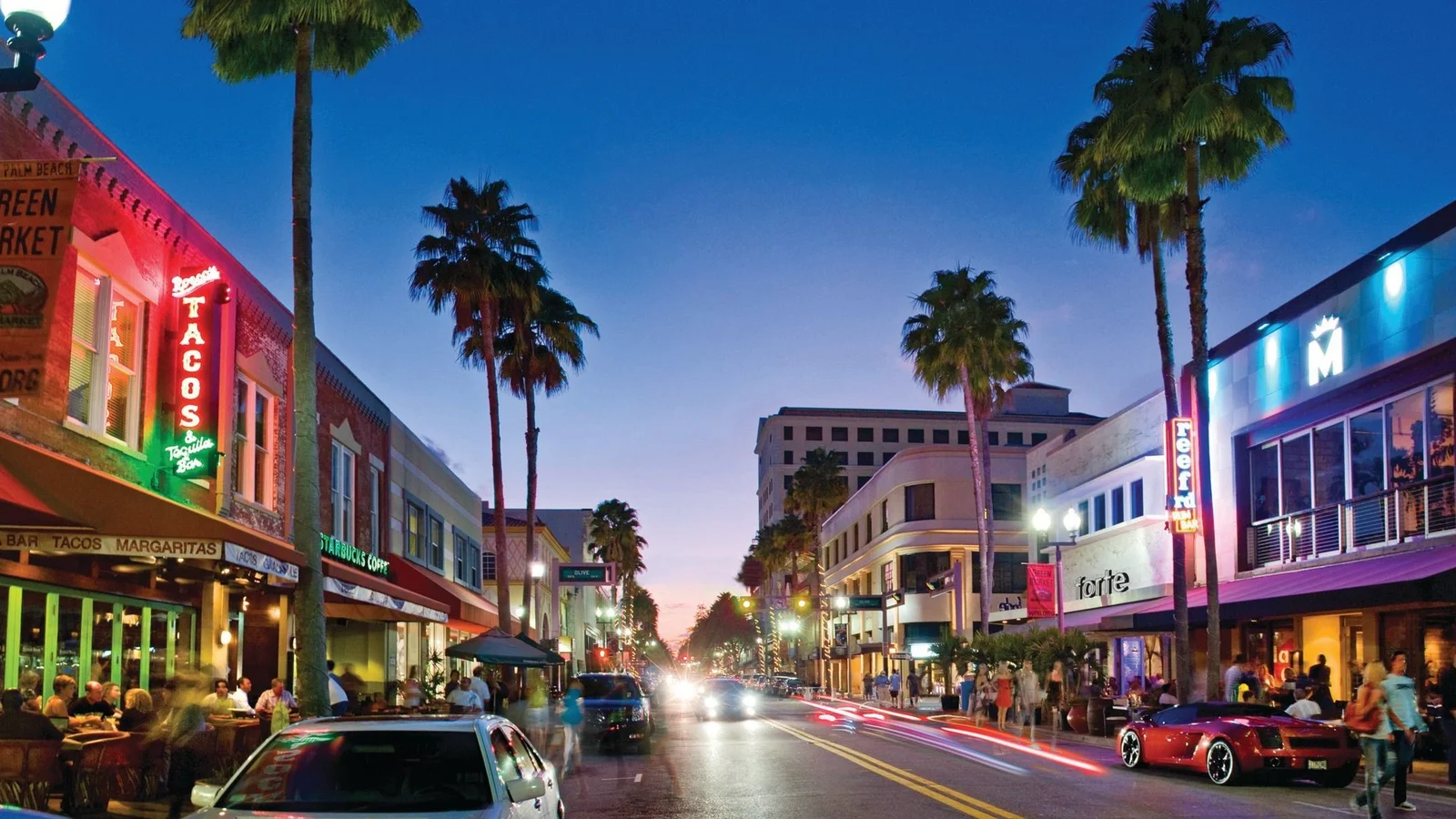 Downtown shops and restaurants along a palm-lined street at dusk in the Palm Beaches