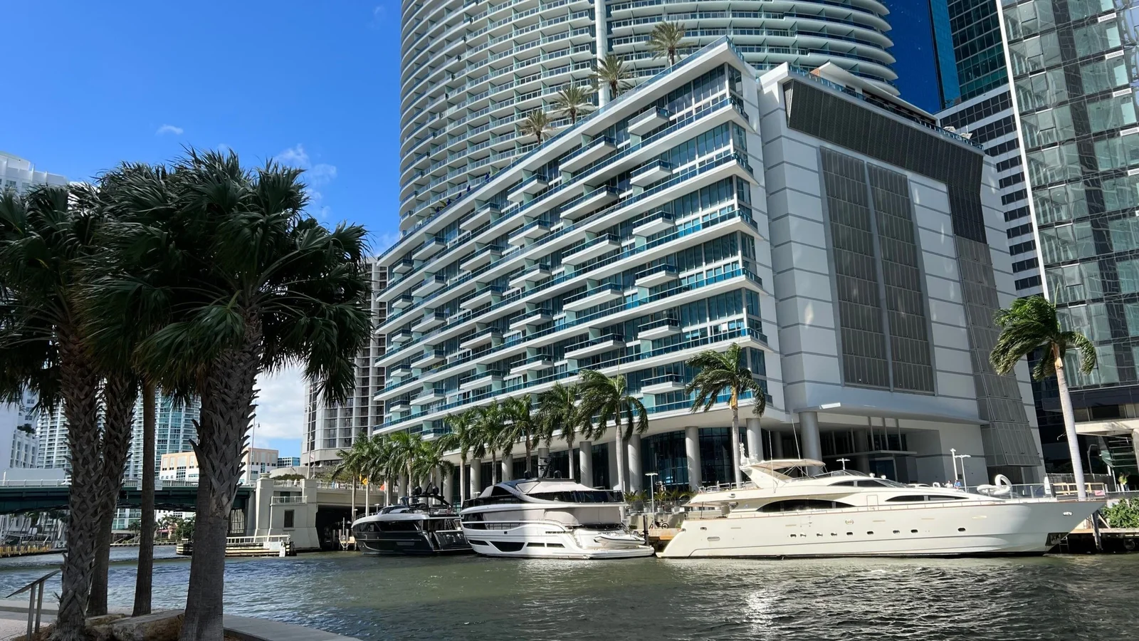 The Epic Residences and Hotel building on the Miami River, with stepped balconies above palm trees and yachts moored along the riverwalk.