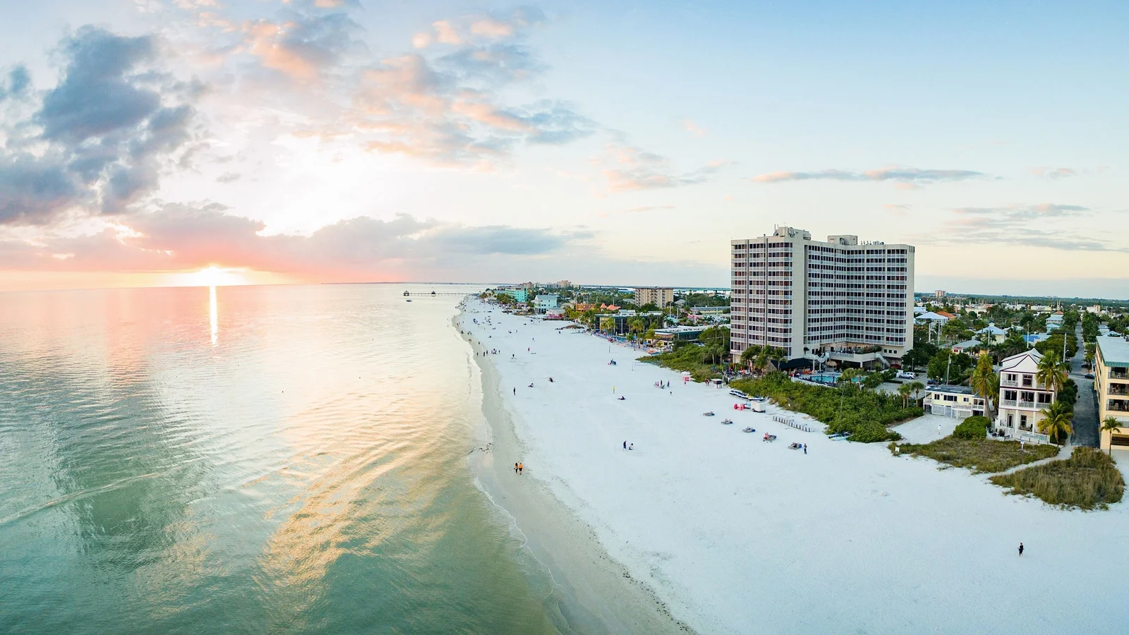 Aerial view of a beachfront condo tower and white sand beach on Fort Myers Beach at sunset.
