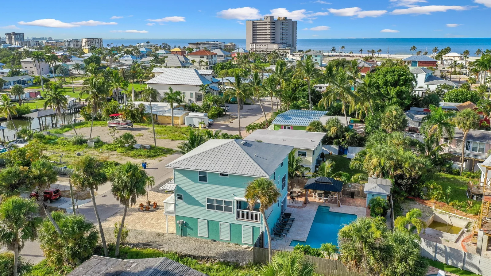 Aerial view of single-family homes with pools among palms on Fort Myers Beach, with the Gulf beyond.