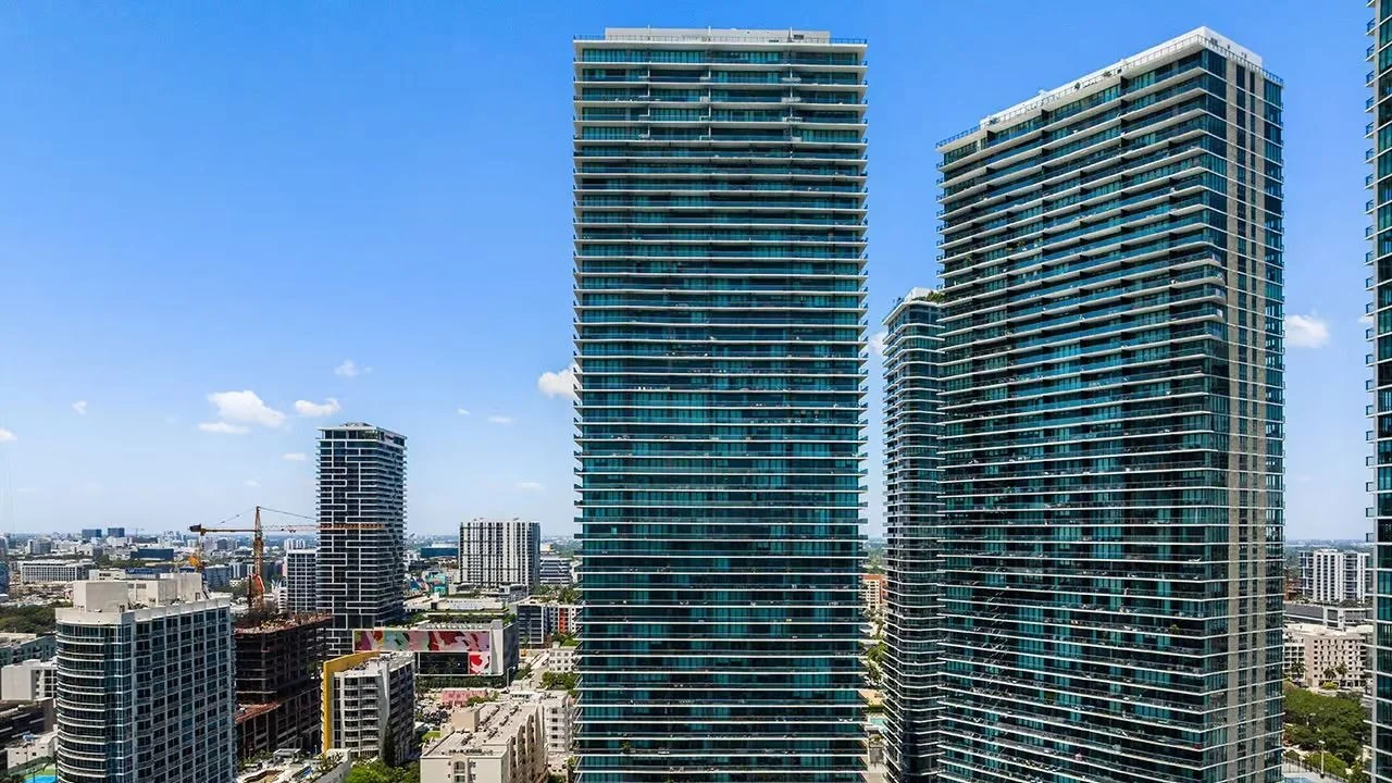 The glass Gran Paraiso tower at the centre, beside another Paraiso District tower in Edgewater, under a clear blue sky.