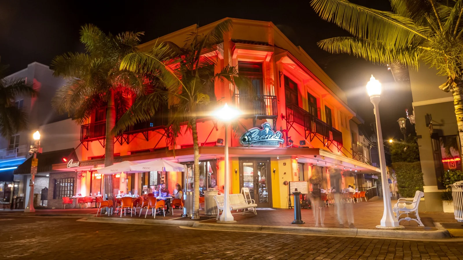 Illuminated corner building with palms on a downtown Fort Myers street at night.