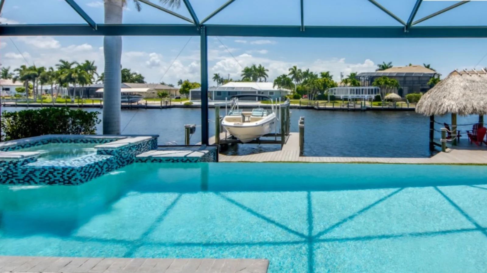 Pool deck of a canal-front home with a boat dock and waterfront houses in the Fort Myers area.