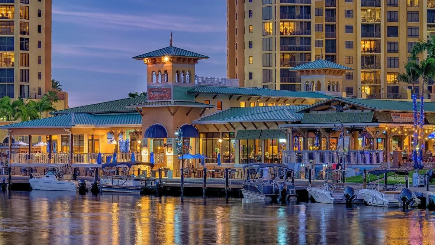 Waterfront restaurant and high-rise condos at a marina in Cape Coral at dusk.
