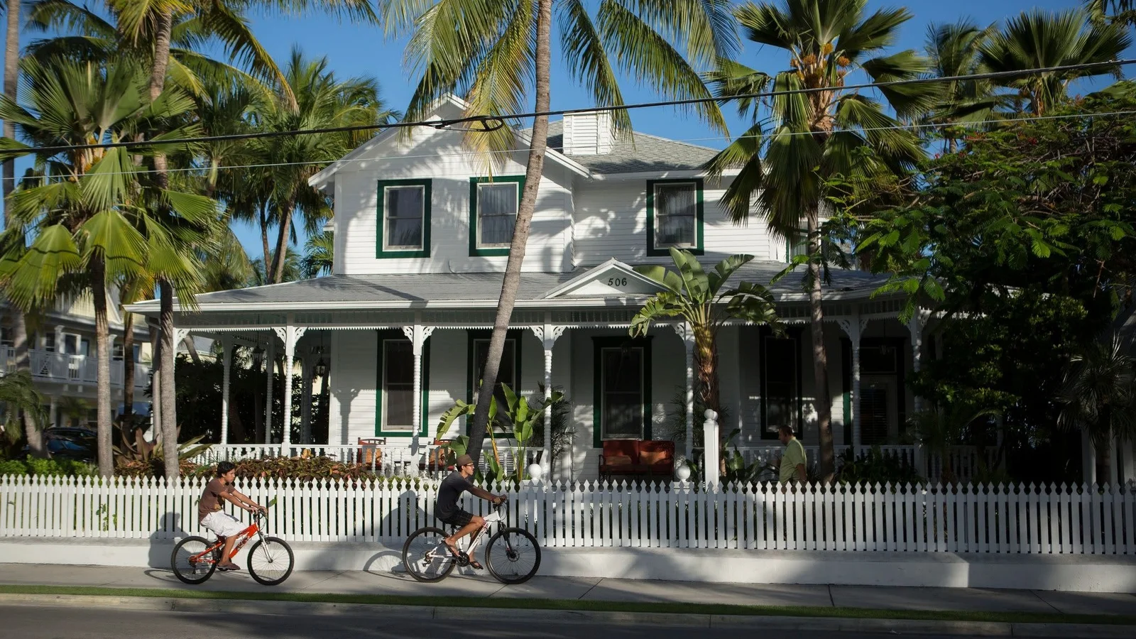 Cyclists passing a white wooden house with a picket fence in Old Town Key West