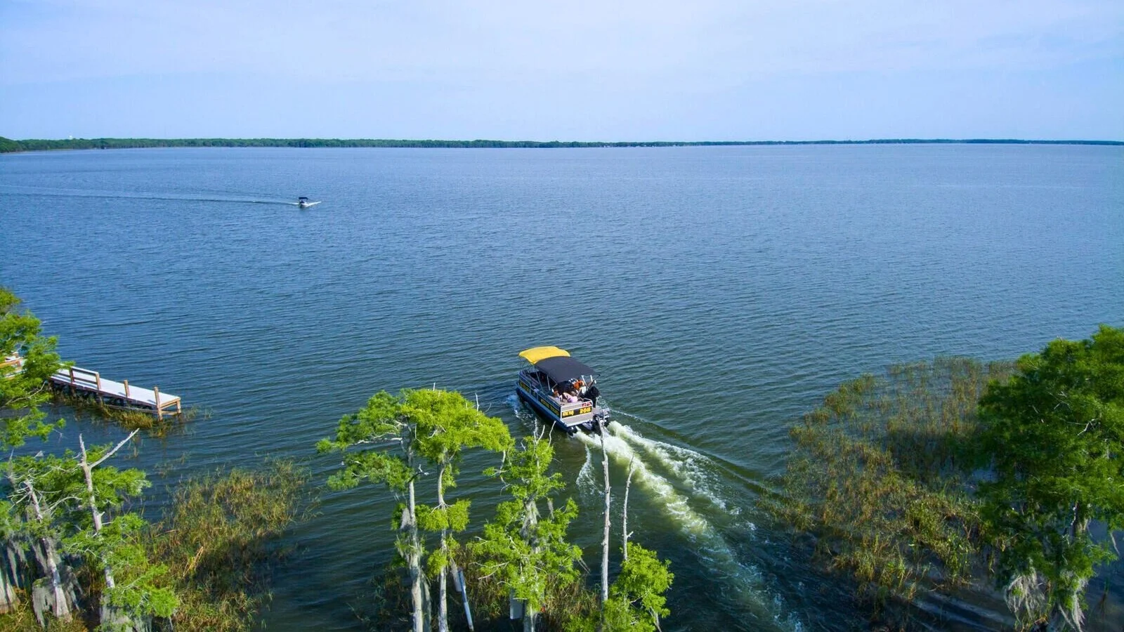 Aerial view of a boat heading from a cypress-lined canal onto open lake water in Lake County.