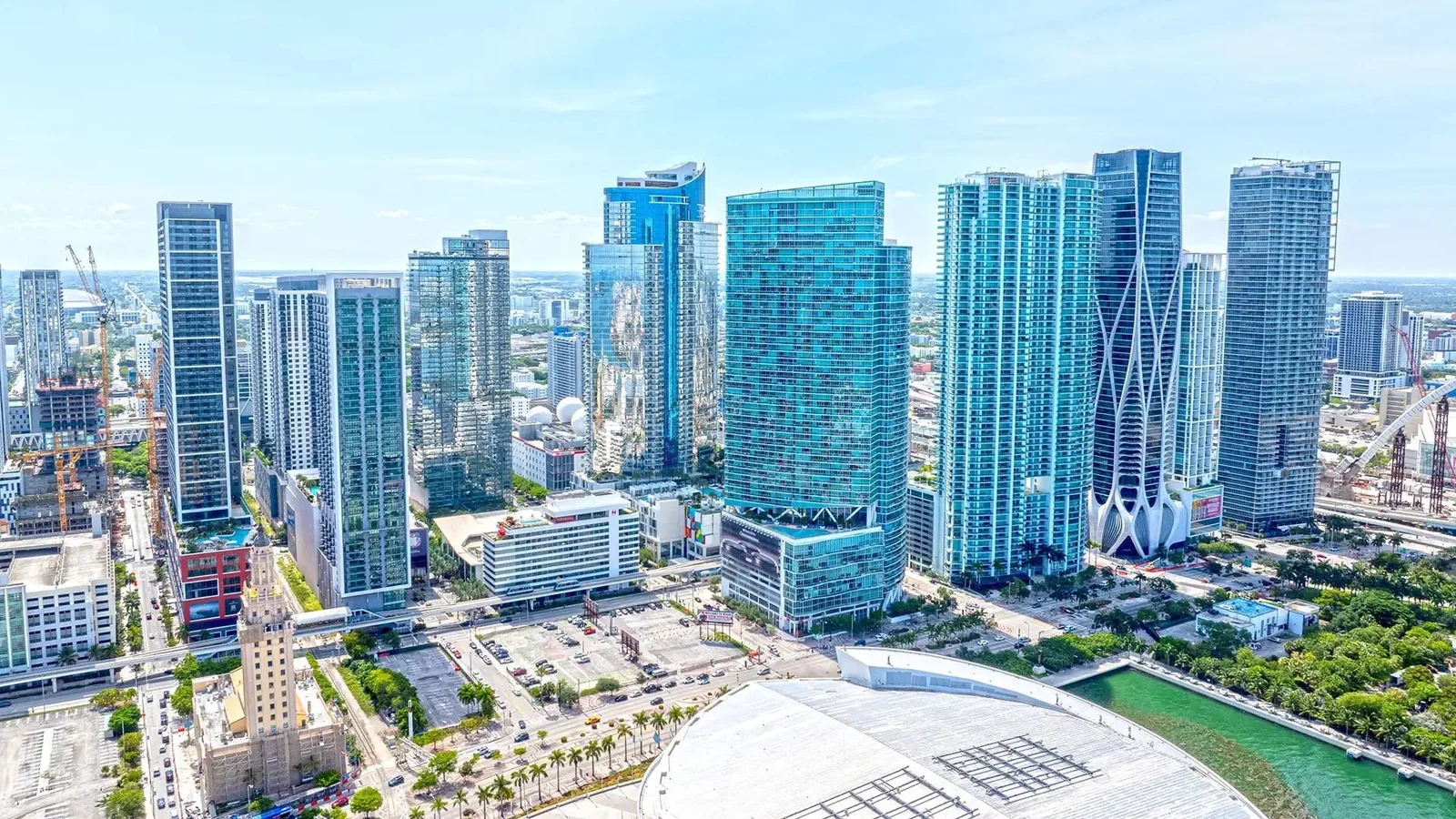 Aerial view of the Miami Worldcenter area of Downtown Miami, with glass residential towers rising behind the Freedom Tower and the white roof of the Kaseya Center.