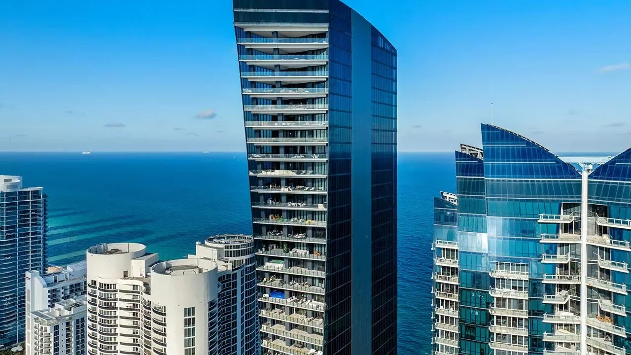 Dark glass tower of Muse Sunny Isles between neighbouring oceanfront towers, with the Atlantic behind