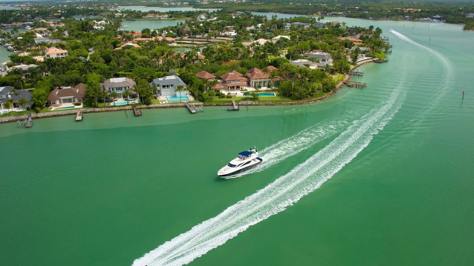 Motor yacht cruising past waterfront homes and private docks on a waterway in Naples