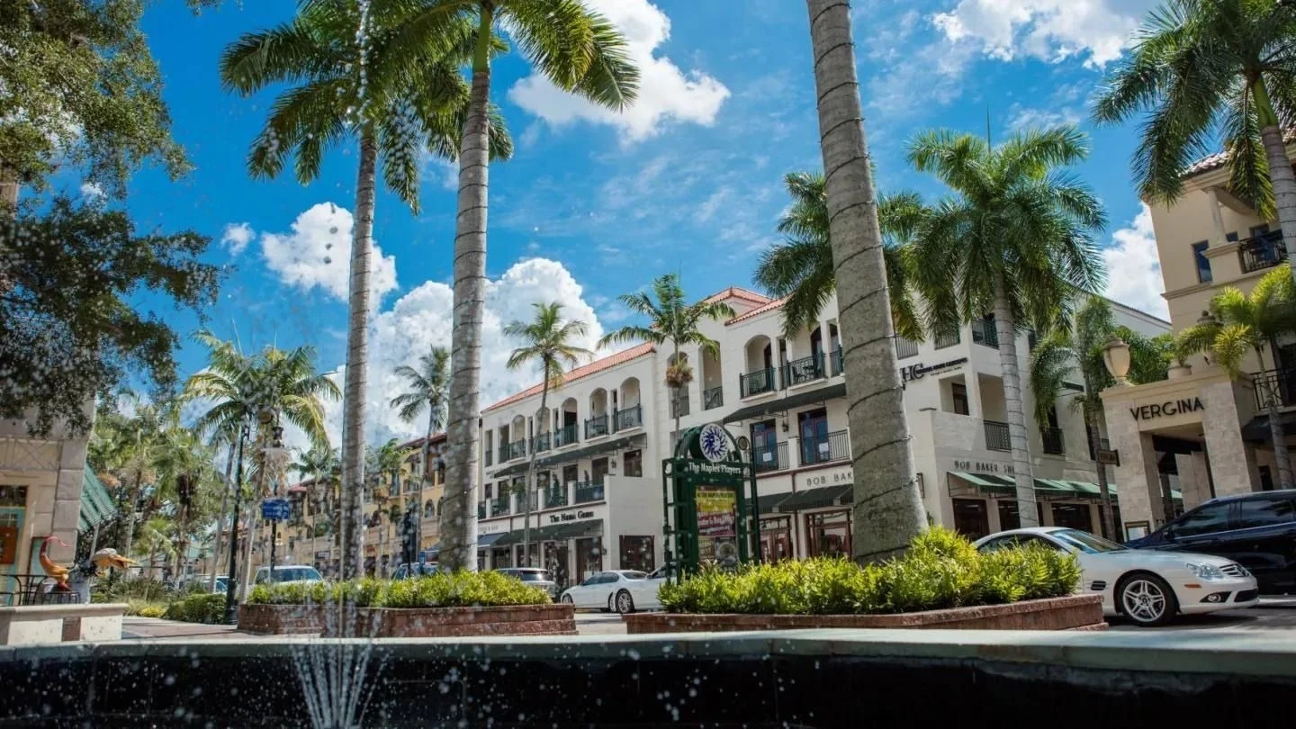 Palm-lined street with shops and a fountain in downtown Naples, Florida.
