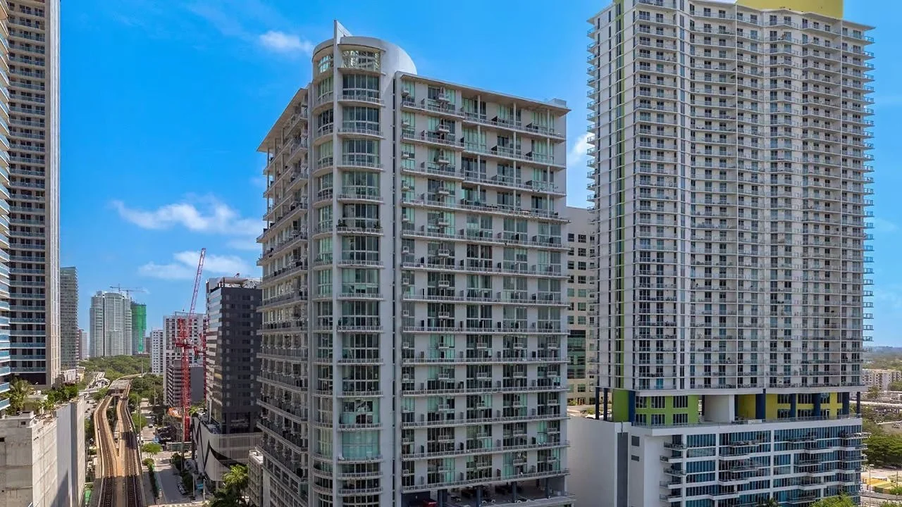 The Neo Vertika condo tower beside a neighbouring high-rise near the Miami River, under a blue sky.
