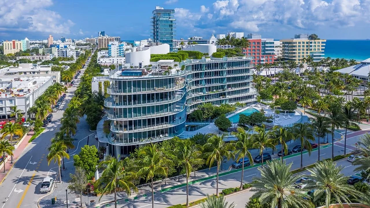 Aerial view of the curved glass mid-rise of One Ocean on a palm-lined street in South of Fifth