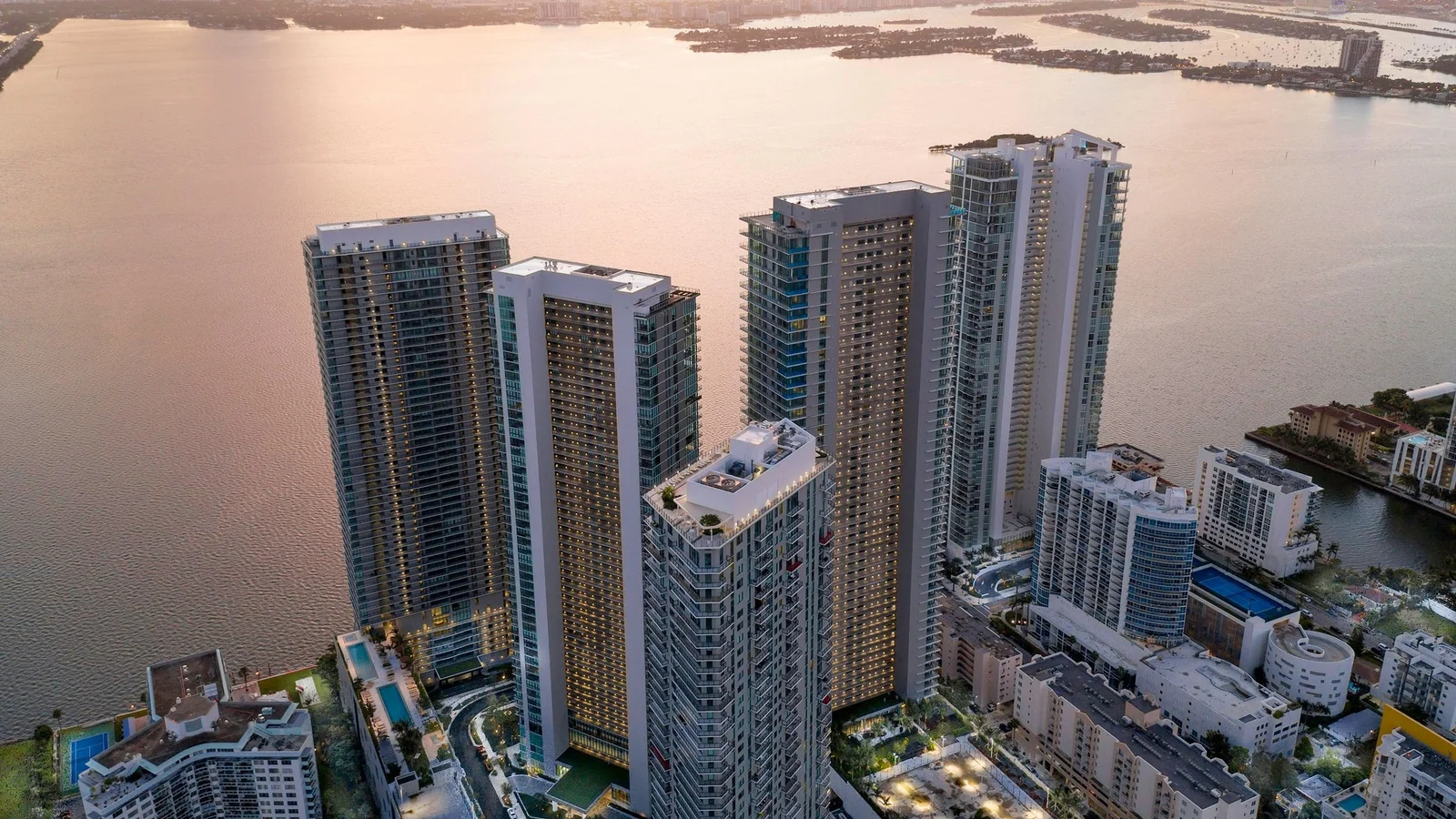 The Paraiso District towers in Edgewater, including One Paraiso, seen from above at dusk beside Biscayne Bay.