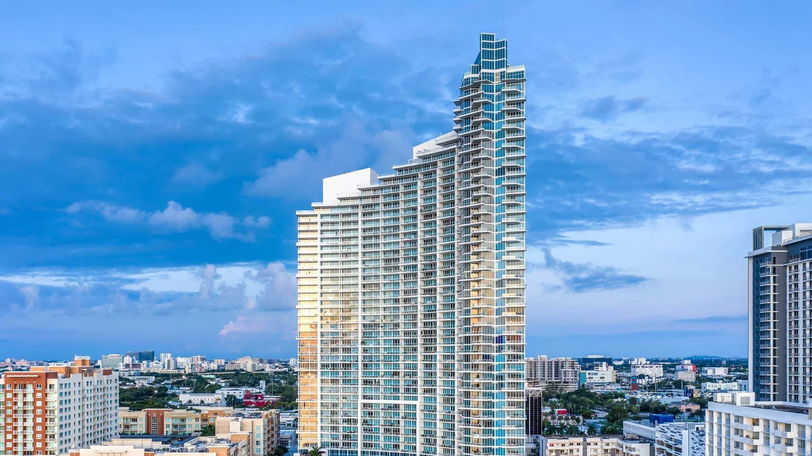 The white Paramount Bay tower in Edgewater with its stepped, sloping crown against a blue evening sky.