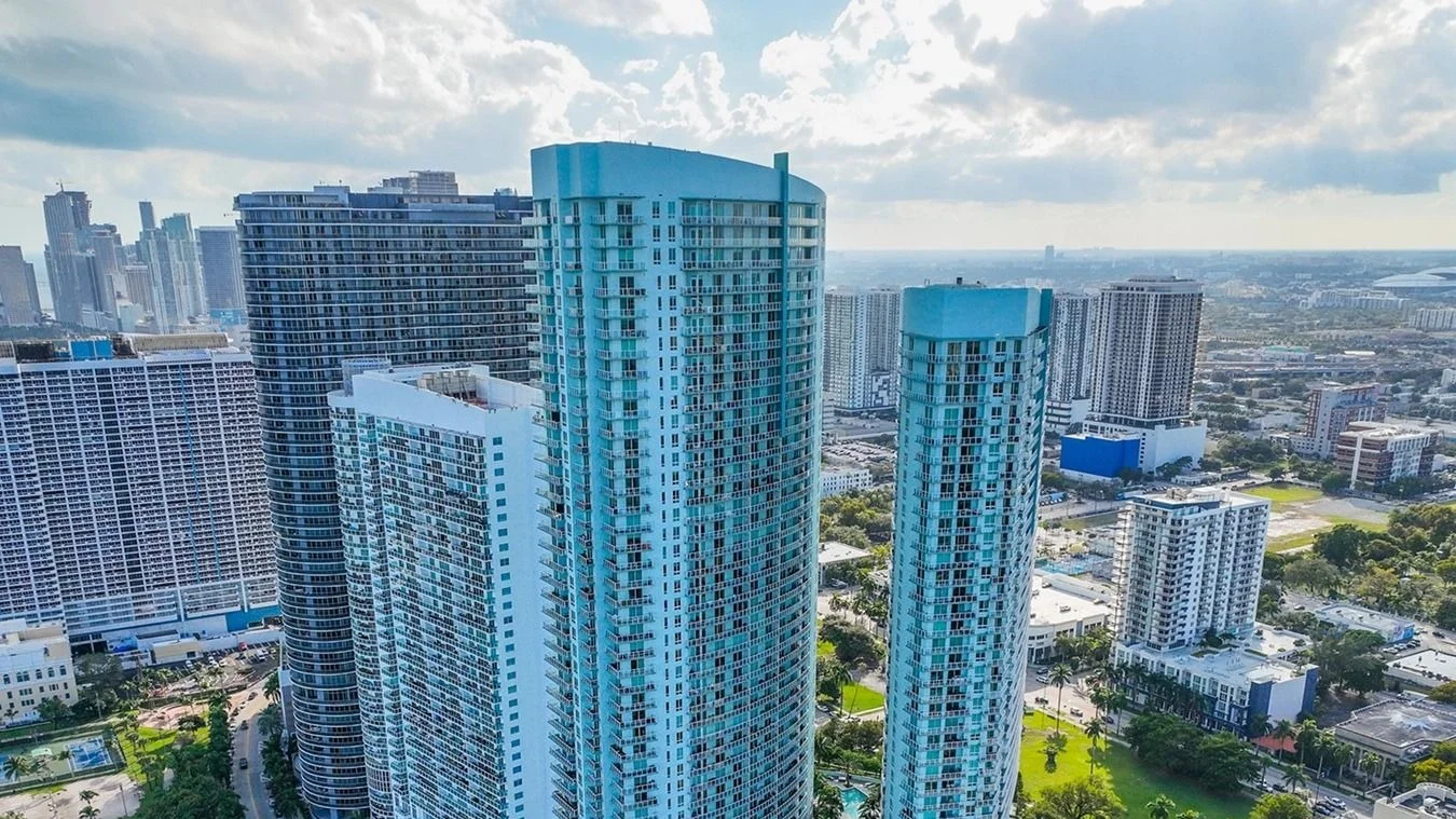 The two blue glass towers of Quantum on the Bay in Edgewater seen from above, with neighbouring high-rises and the city behind.