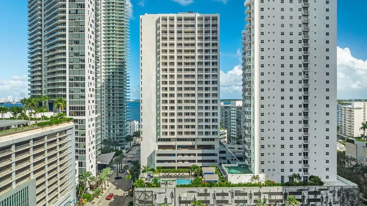 The Sail on Brickell condo tower standing between neighbouring Brickell towers, with the bay in the distance.
