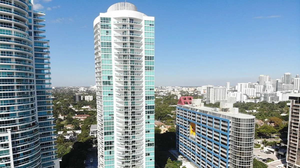 The slim Skyline on Brickell tower rising above low-rise Brickell buildings, with Coconut Grove greenery behind.