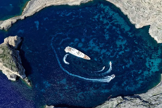 Superyacht at anchor in a rocky bay with two tenders circling