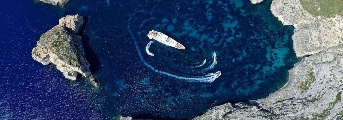 Superyacht at anchor in a rocky bay with two tenders circling