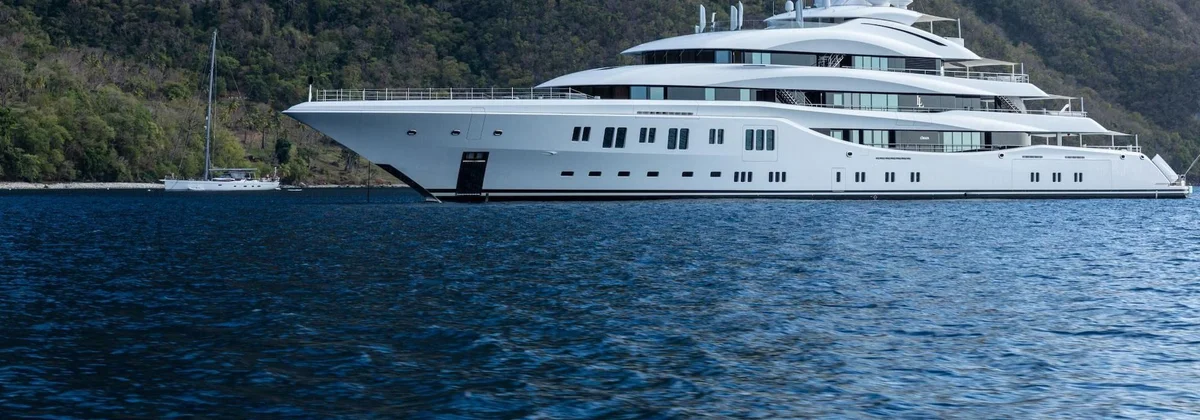 Superyacht at anchor below a steep green mountainside