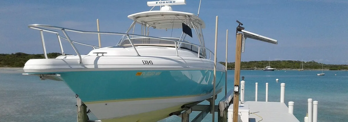 Centre console boat raised on a boat lift beside a dock in clear water