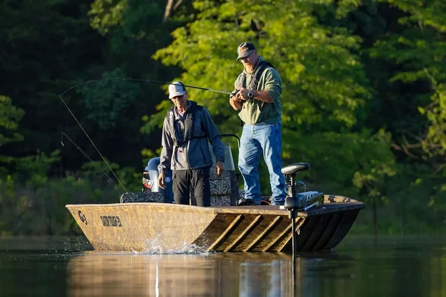 Two anglers fishing from a camouflage aluminium jon boat on a wooded lake