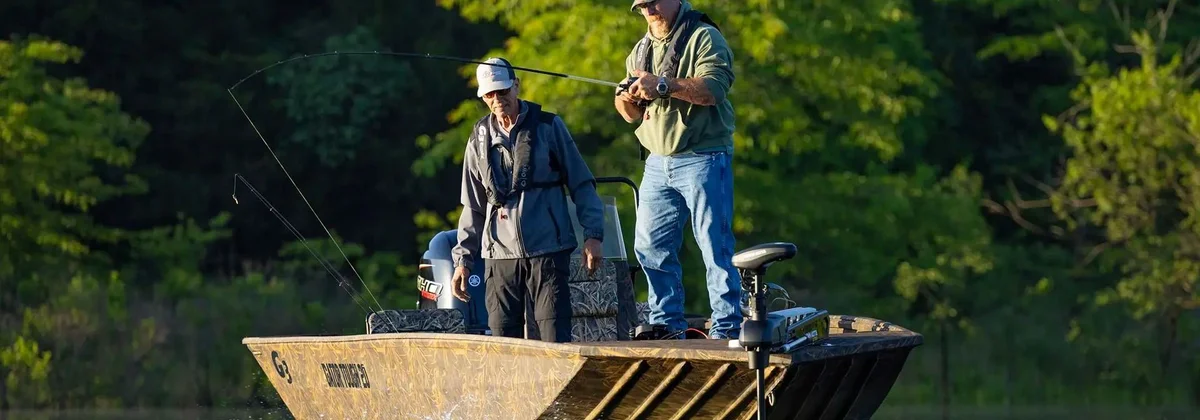 Two anglers fishing from a camouflage aluminium jon boat on a wooded lake