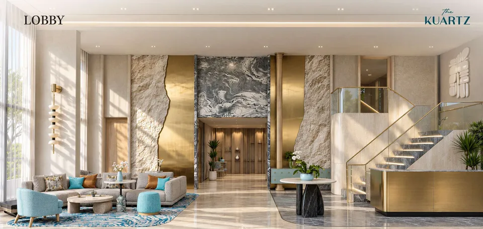 Double-height lobby of The Title KUARTZ with stone and brass walls, a lounge area and a glass staircase